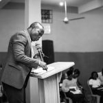 man in brown suit standing in front of table