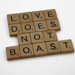 Scrabble tiles arranged to spell 'Love Does Not Boast' on a white surface.