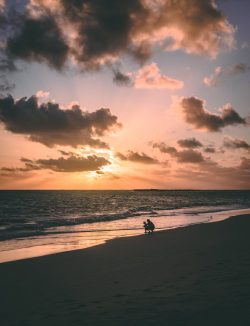 A stunning silhouette of a father and child on a beach during a vibrant sunset.