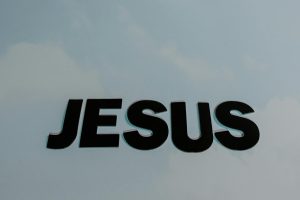 Typography displaying 'JESUS' against a soft cloudy sky background, focus on text.