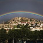 Vibrant rainbow arches over a picturesque hillside town, capturing a moment of natural beauty.