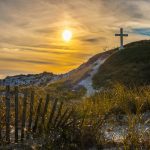 white cross on grass covered hilltop during sunrise
