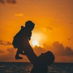 silhouette photo of man carrying baby during golden hour