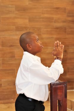 a young boy in a white shirt and black pants praying