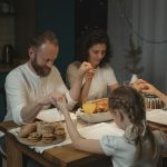 Family holding hands and praying over a dinner table with turkey and cookies during festival celebration.