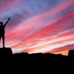 silhouette of man standing on high ground under red and blue skies